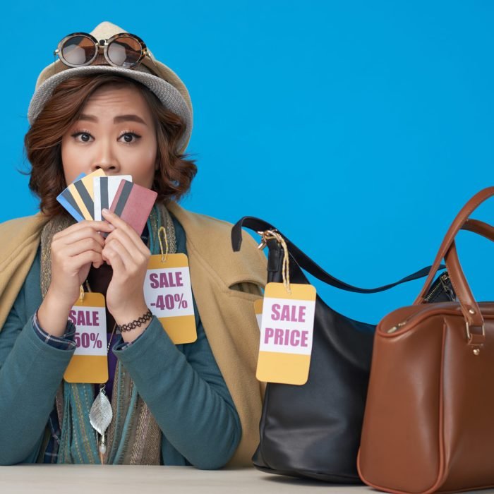 Woman addicted to shopping holding lots of credit cards on blue background